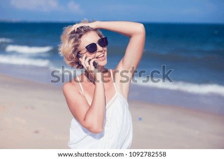 Young happy woman talking on mobile phone on a beach with sea background