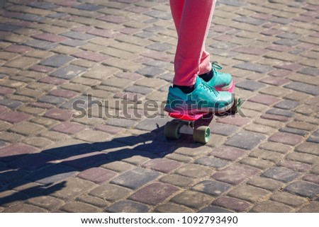 young skateboarder legs in pink tights and blue sneakers skateboarding at skate park