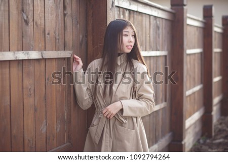 Portrait of a young Asian woman in a coat close-up near a wooden wall