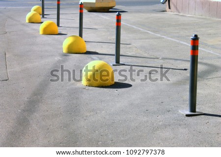 Gray parking poles with red reflective strips and yellow hemispheres separating the sidewalk from the road