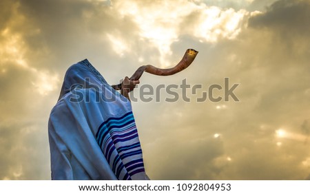 Blowing  the shofar for the Feast of Trumpets - Jewish man in a tallit prayer shawl against dramatic sky Royalty-Free Stock Photo #1092804953