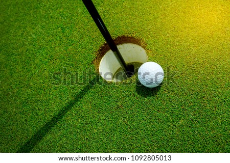 White golf ball near the hole on the green grass at summer - leisure activity