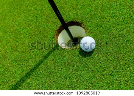 White golf ball near the hole on the green grass at summer - leisure activity
