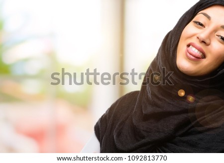 Young arab woman wearing hijab sticking out tongue at camera at sign of disobedience, protest and disrespect