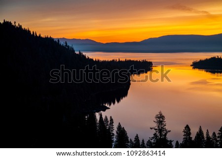 Brilliant golden reflections on Lake Tahoe sunrise shines across majestic waters and Sierra Nevada Mountains along pine forests and perfect landscape at Emerald Bay , Lake Tahoe , California , USA