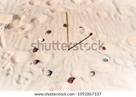 Sundial on the beach made of a stick and stones. Royalty-Free Stock Photo #1092867107
