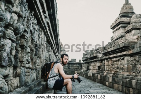 Handsome young tourist feeling the peace and taking some pictures of the great Borobudur temple, historical famous place in the java island Indonesia. Lifestyle and travel photography.
