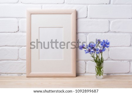 Wooden frame mockup with blue cornflower in the simple glass vase. Empty frame mock up for presentation design. Template framing for modern art.