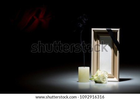 Blank brown mourning frame, with smoky candle and white rose, on dark background with red decoration