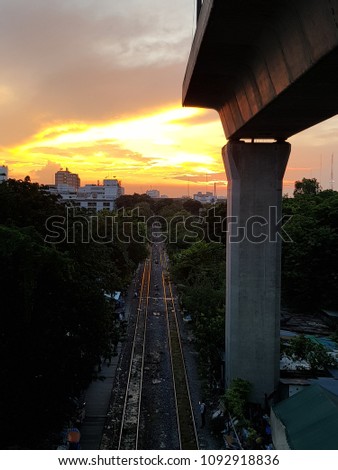 High angle view of a dark and endless train rail way track under incompleted skytrain construction with sunset background. Silhouette sutset at the evening in city. Transportation, building concept.