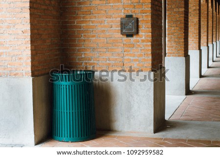 A green metal trash can and wooden no smoking sign on industrial loft style red brick and concrete wall and floor.