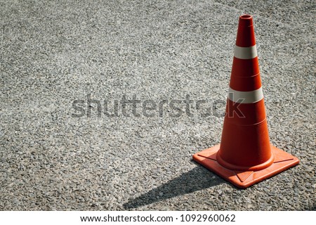 An orange and white stripes traffic cone with shadow from the sunlight on the concrete surface of the parking lot. Copy space.