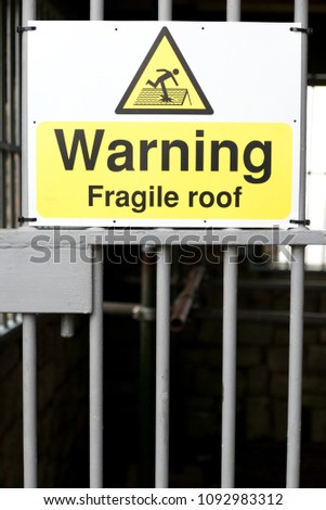 Warning fragile roof sign black text on yellow and white background with symbol of man stepping on and breaking roof 