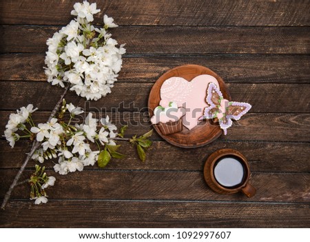 Top view image of cherry blossom  flowers and ginger biscuits next to cup of coffee on rustic wooden table.