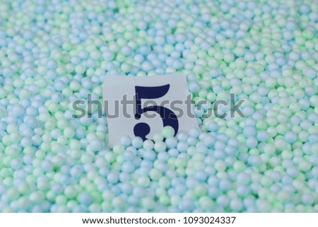 The number 5 of the piece of paper in a pile of small spheres