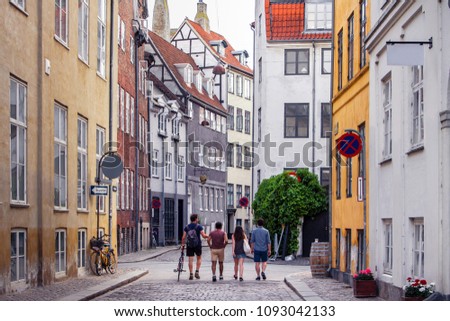 Beautiful bright cityscape in perspective. View on cobbled street with bicycles. Narrow street with colorful buildings in old historic center of Copenhagen. Red tiled roofs. Four people men go forward Royalty-Free Stock Photo #1093042133