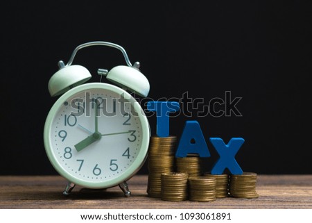 Time to pay TAX concept. TAX alphabet with stack of coin and vintage alarm clock on wooden working table in dark background, business and financial concept idea.