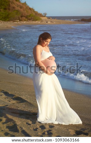 Pregnant woman in white dress standing on beach background