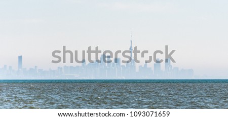 Distant city skyline silhouette of Toronto downtown in fog and mist with wavy water of Lake Ontario in foreground.