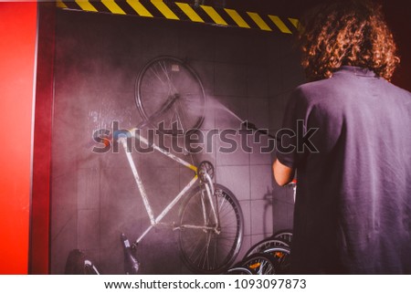 Services professional washing of a bicycle in the workshop. Close-up of hand Young Caucasian stylish man doing bicycle cleaning using automatic electric water pump. Sprays scatter from the pressure.
