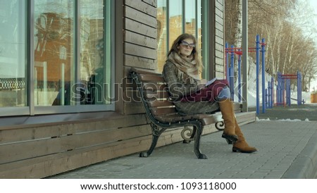 young, beautiful, lovely woman sitting on bench in park, in hands of her notebook. She is wearing a coat. She makes notes and looks very romantic.4k