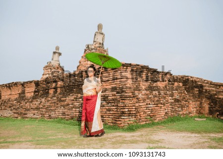 Woman put Traditional Thai Costumes green umbrella at Wat Chaiwatthanaram with blurry people background.
