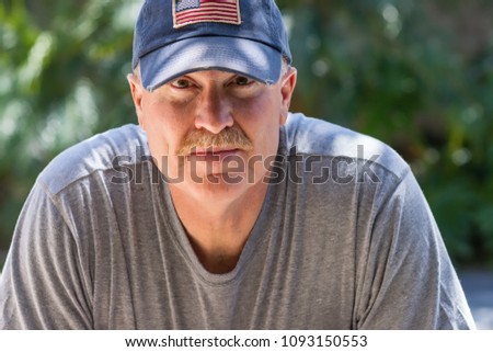 Older male wearing USA flag baseball hat in serious look outdoors