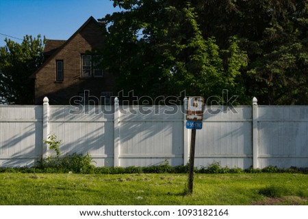 Old rusted street sign with with white fence and grass in background.