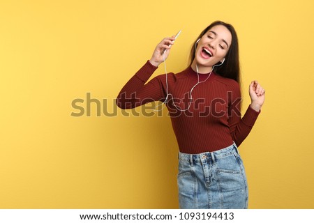 Young woman using phone for listening to music on color background