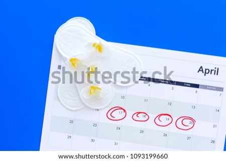 Menstruation cycle concept. Menstruation calendar with sanitary pads and delicate flowers on blue background top view copy space