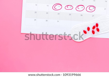 Menstruation cycle concept. Menstruation calendar with sanitary pads and contraceptive pills on pink background top view copy space