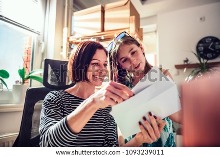 Mother and daughter sitting by the window and checking mail together at home office Royalty-Free Stock Photo #1093239011