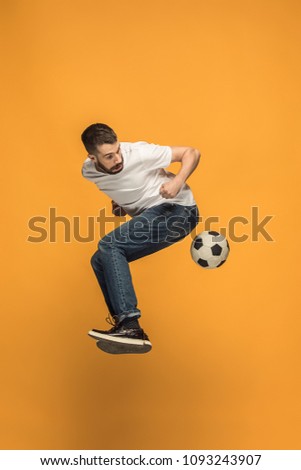 Forward to the victory.The young man as soccer football player jumping and kicking the ball at studio on a yellow background. Football fan and world championship concept. Human emotions concepts