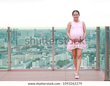 Portrait of happy pregnant mother posting on the rooftop building.