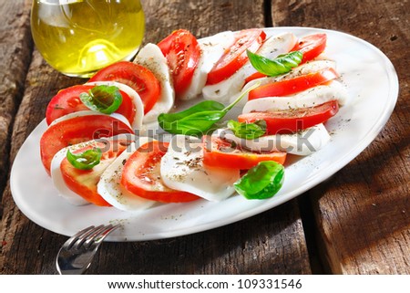Colourful slices of cheese and tomato arranged alternately on a plate and garnished with herbs served with an oil dressing for drizzling