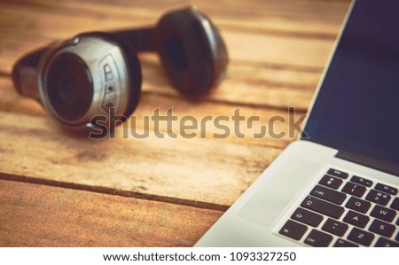 A 45 degree view of a set of wireless headphones and laptop lying on a rustic wood table, desk. 
