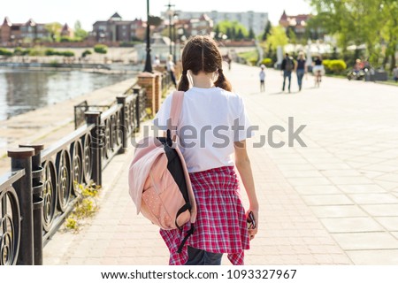 Teenage student girl walking down the street with backpack. Back to school, back view.