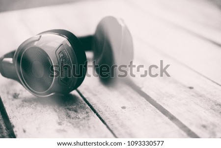 A 45 degree view of a set of wireless headphones lying on a rustic wooden table outside. 