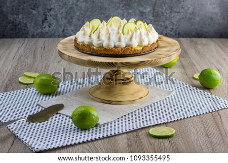 Lime meringue cake on wooden plate with slices of lime on wooden board and marble background