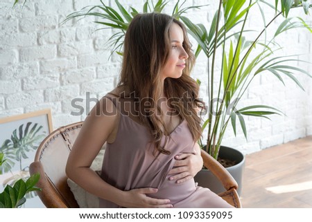 Pregnant girl sitting in a chair on a white brick background.