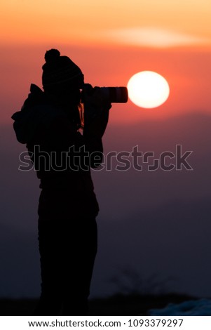 Young women photographer trying to capture the sunrise through her camera