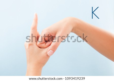 Fingerspelling alphabet. Female hands isolated on blue background showing deaf mute BSL alphabet letter K.