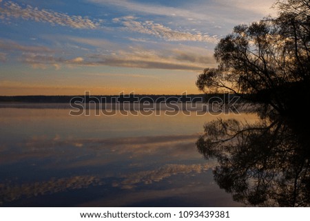 Dawn over the quiet water surface of the lake. The morning blue sky is lit by the orange light of the sun. Soft colors, the sky is reflected in the water.