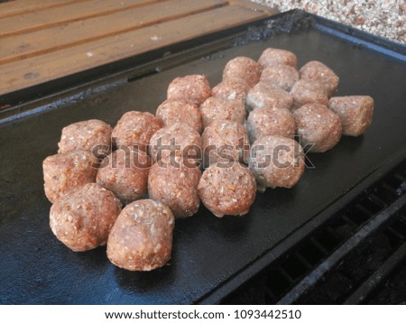 Close up of raw round meatballs cooking on a hot barbecue 