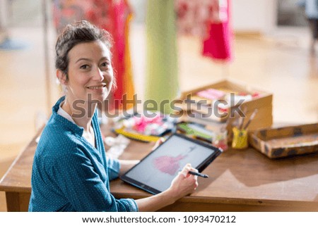 Looking at camera a Fashion designer working on a new model in her studio, she designs a new dress on a digital tablet