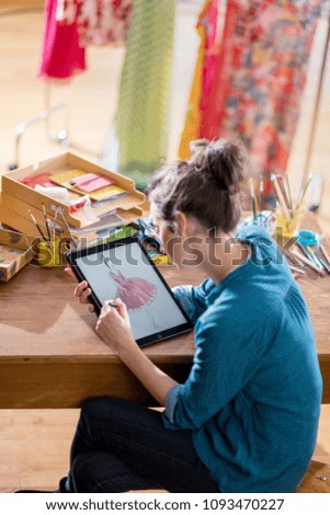 Fashion designer working on a new model in her studio, she designs a new dress on a digital tablet