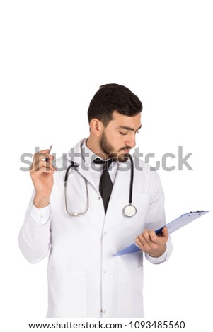 Handsome doctor wearing his coat and stethoscope holding a pen and a paper, he is reading the description, isolated on white background
