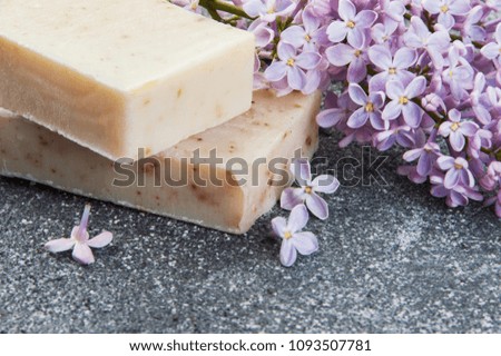 Beige handmade soap scrub and lilac on gray concrete background. Spa setting and copy space for text.