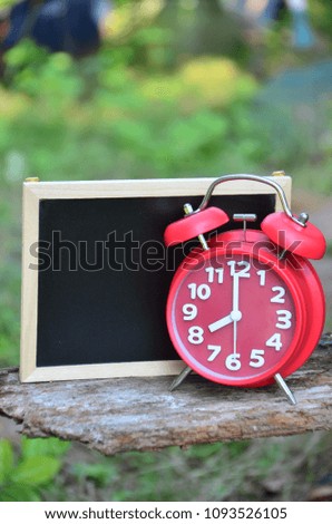 Red clock and blank chalkboard with out of focused garden background