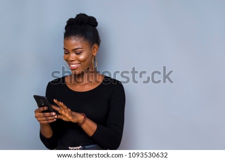 picture of a black african girl on black long sleeves smiling while using her phone  Royalty-Free Stock Photo #1093530632